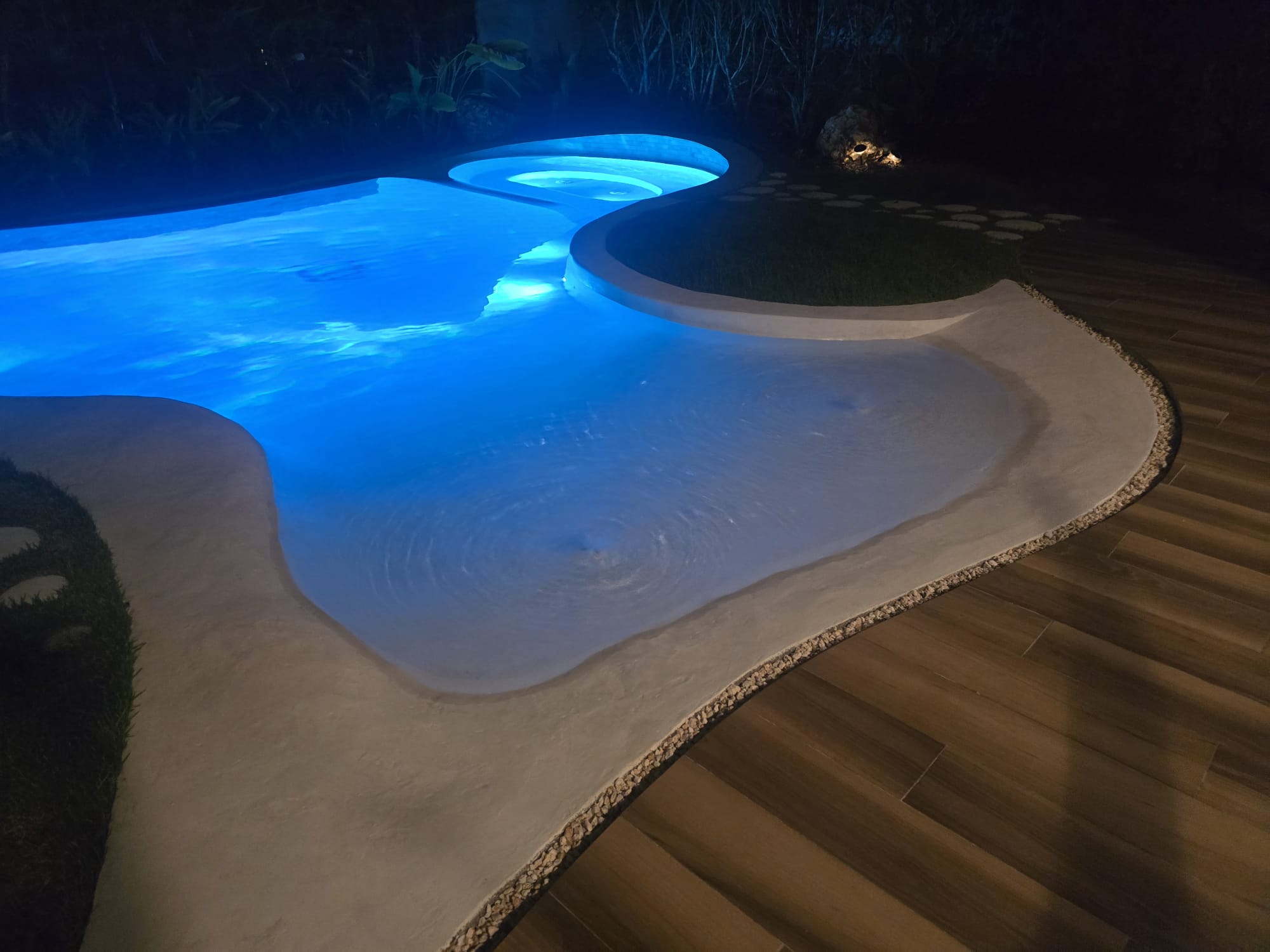 Piscina de formas orgánicas iluminada de noche, por Astacio Pool and Contractors